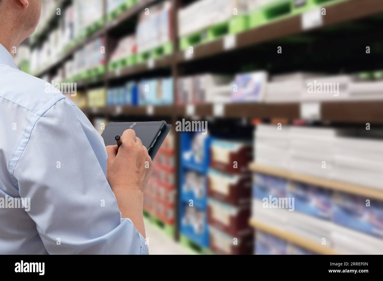 a middle-aged Asian businessman holding a tablet at a warehouse full of goods Stock Photo