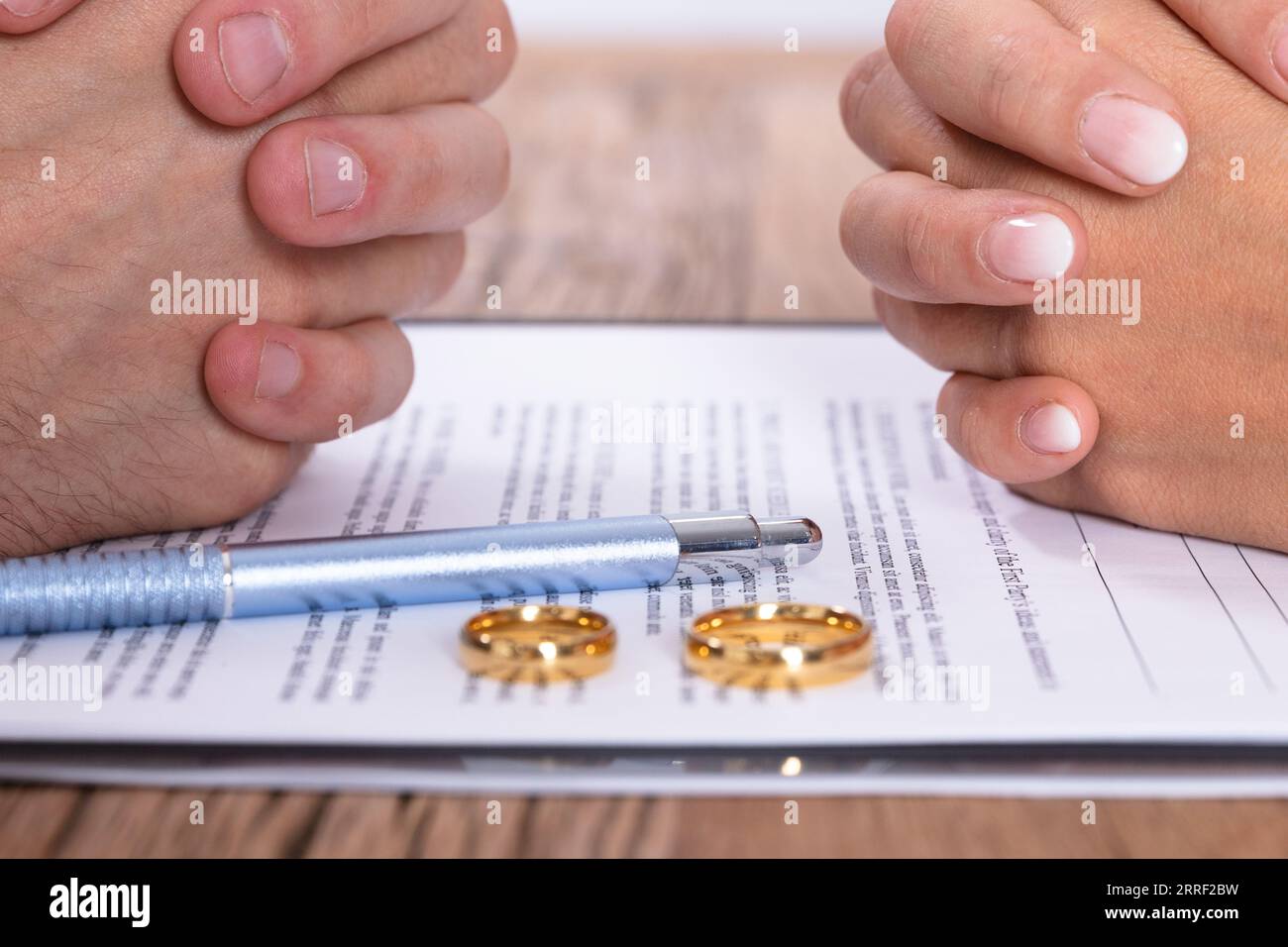 Couple's Hand With Divorce Agreement And Golden Wedding Rings On Wooden