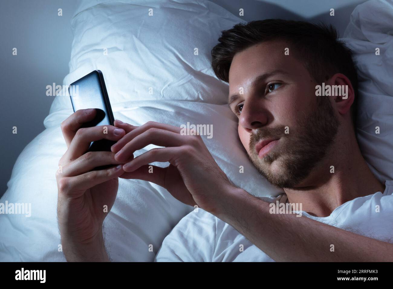 Young Man Using Cellphone In Bed At Night Stock Photo