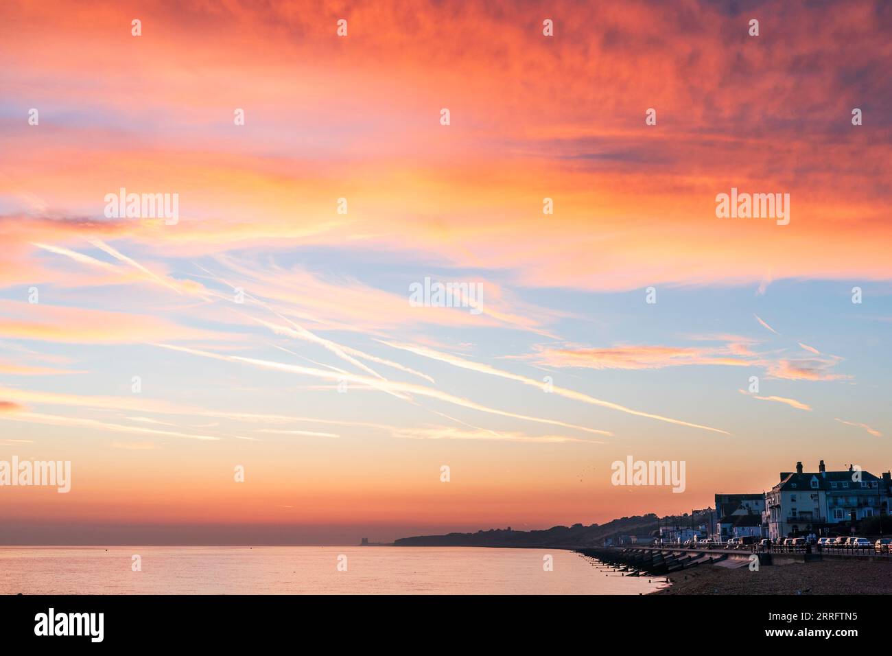 The dawn sky over the seafront at Herne Bay on the north Kent Coast. View along beach and seafront houses with the sea and dawn sky, featuring blue sky and orange reddish clouds. Stock Photo