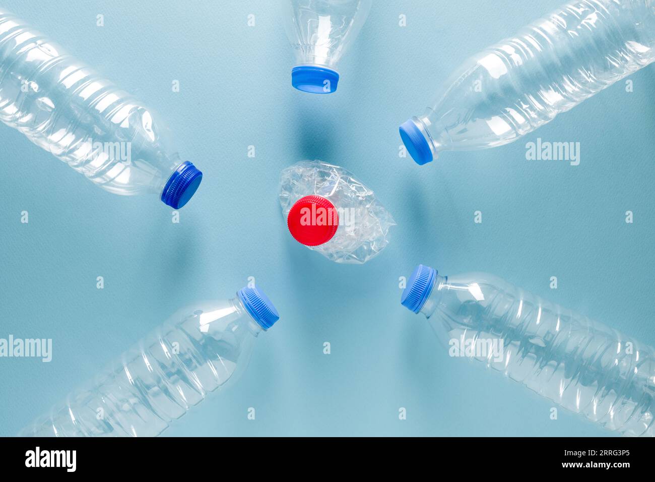 Crushed plastic water bottles with blue caps standing around crushed plastic water bottle with red cap on blue background Stock Photo