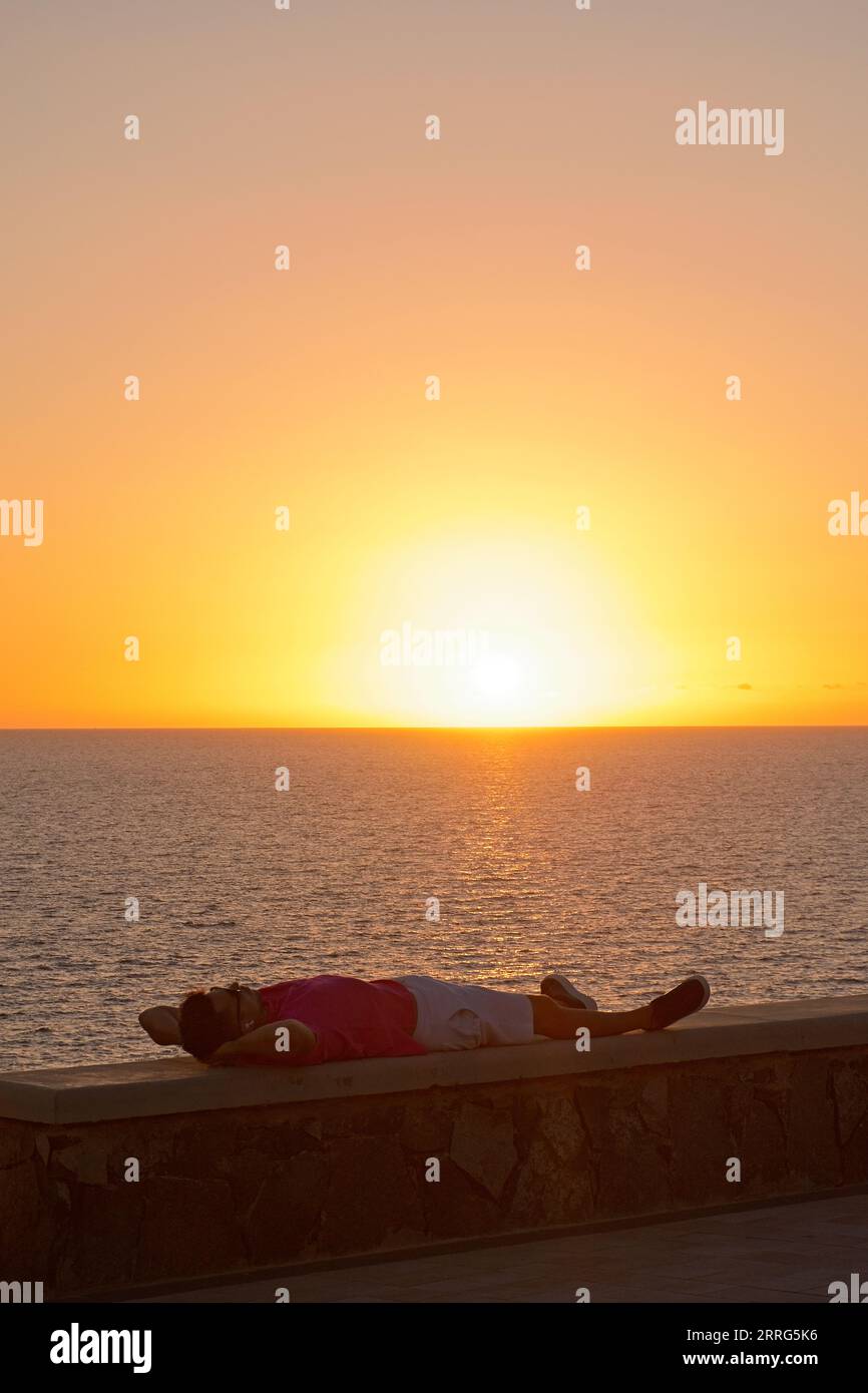 Man's lying down silhouette against sun during sunset in Maspalomas, Gran Canaria, Spain Stock Photo