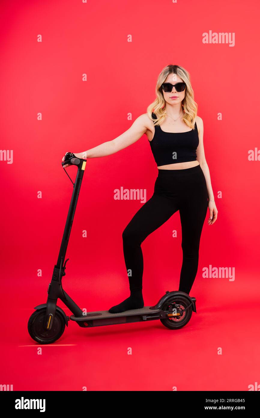 Happy young woman wear glasses riding electric scooter on background studio People lifestyle concept Stock Photo
