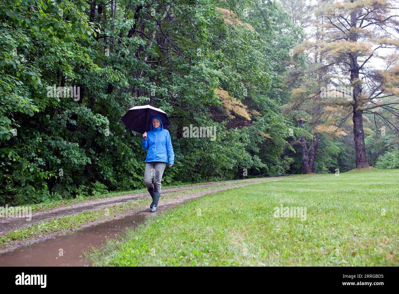 Senior woman happily skipping down muddy trail on rainy day Stock Photo