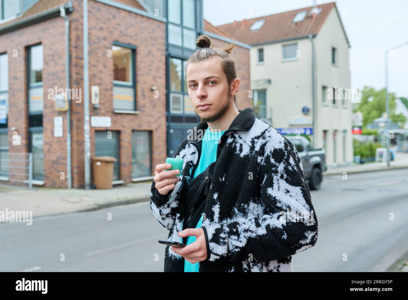 Young hipster male using smartphone, smoking disposable electronic cigarette Stock Photo