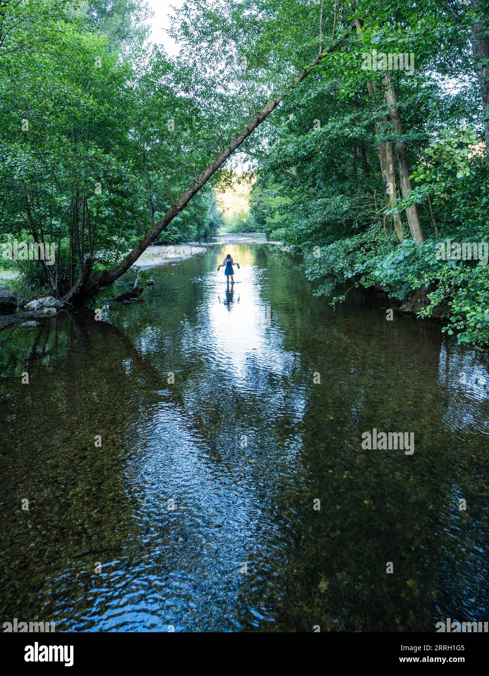 A woman walking with her shoes in her hand through the wild river in the forest. Stock Photo