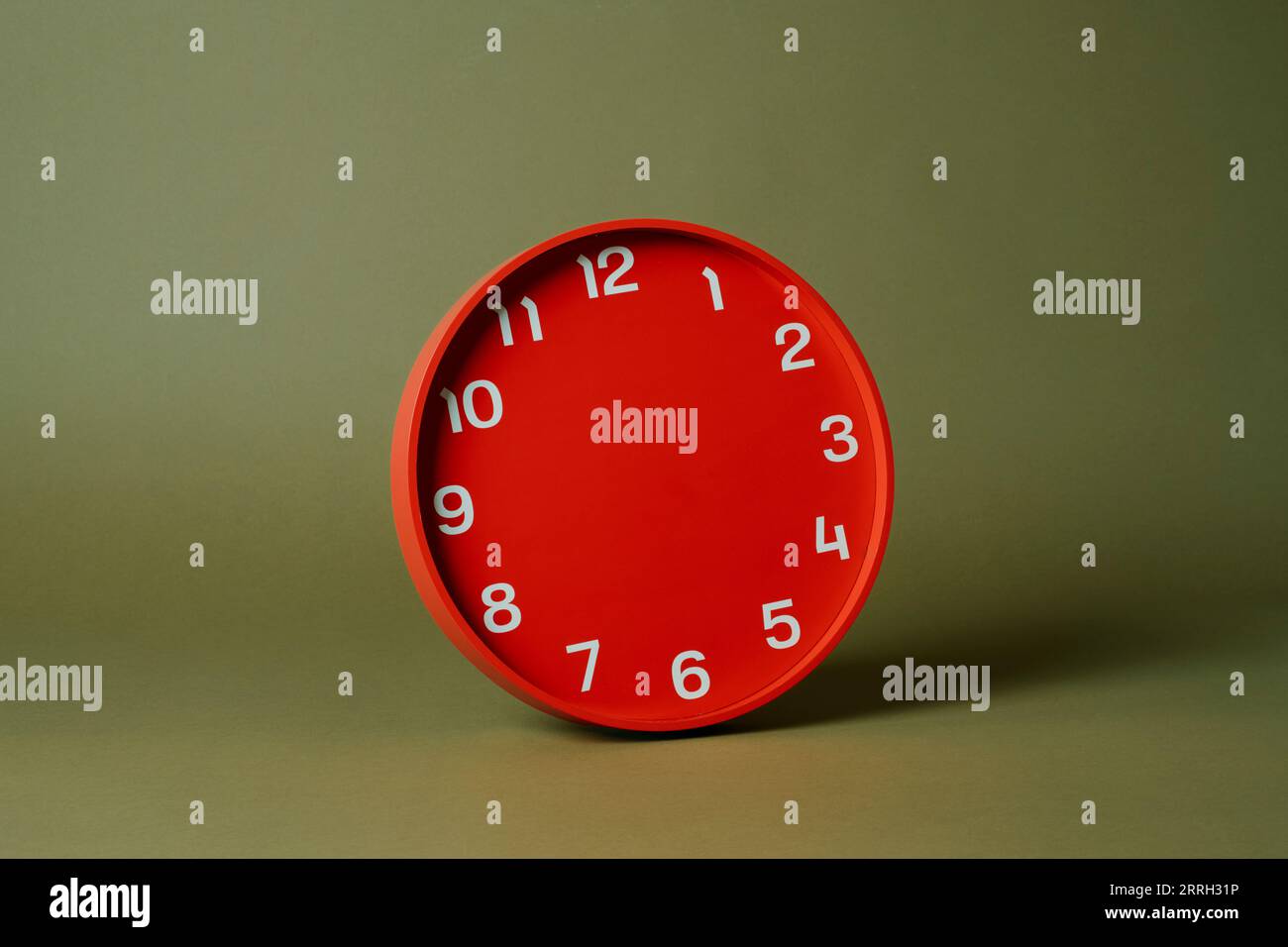 a red clock without any hands on an olive green background Stock Photo