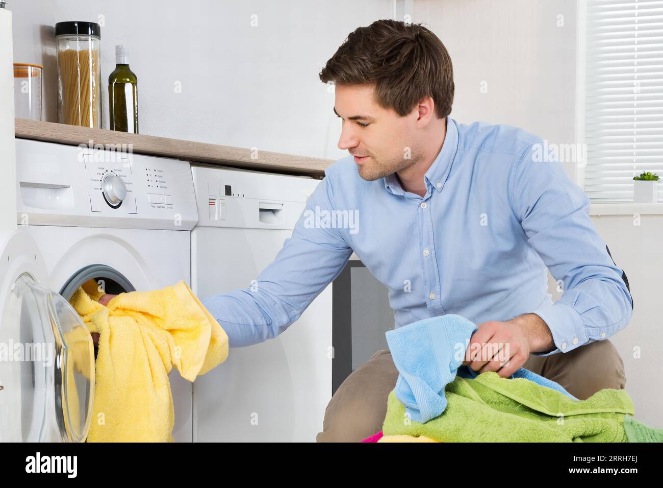 Young Man Loading Clothes Into Washing Machine In Kitchen Stock Photo
