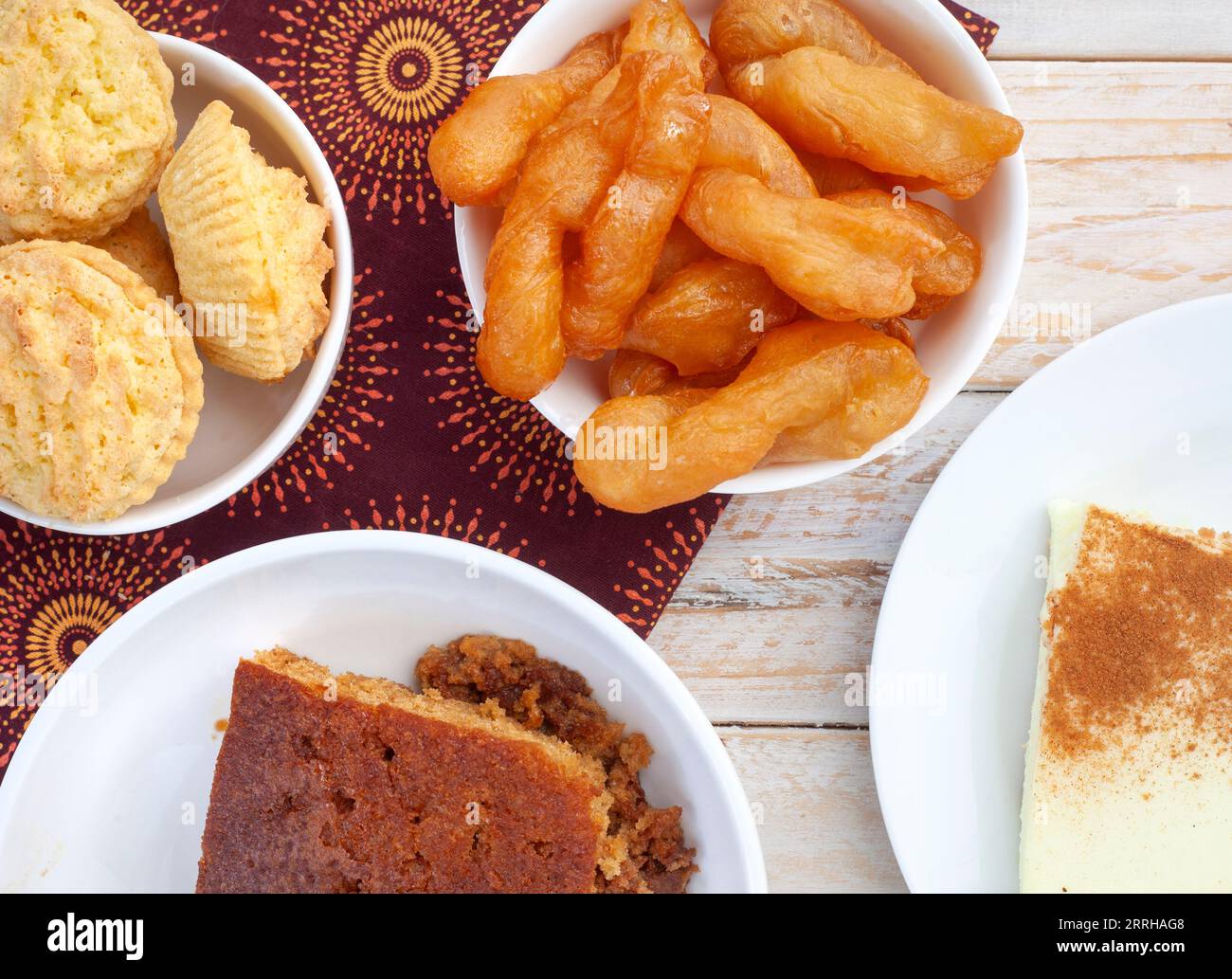 Traditional South African sweet food on rustic wood with traditional printed cloth. Milk tart, koek sisters and malva pudding Stock Photo