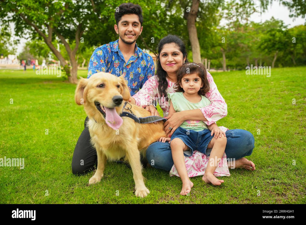 Happy young indian family having fun together at summer park. Mother, father and daughter with labrador dog in garden. Stock Photo