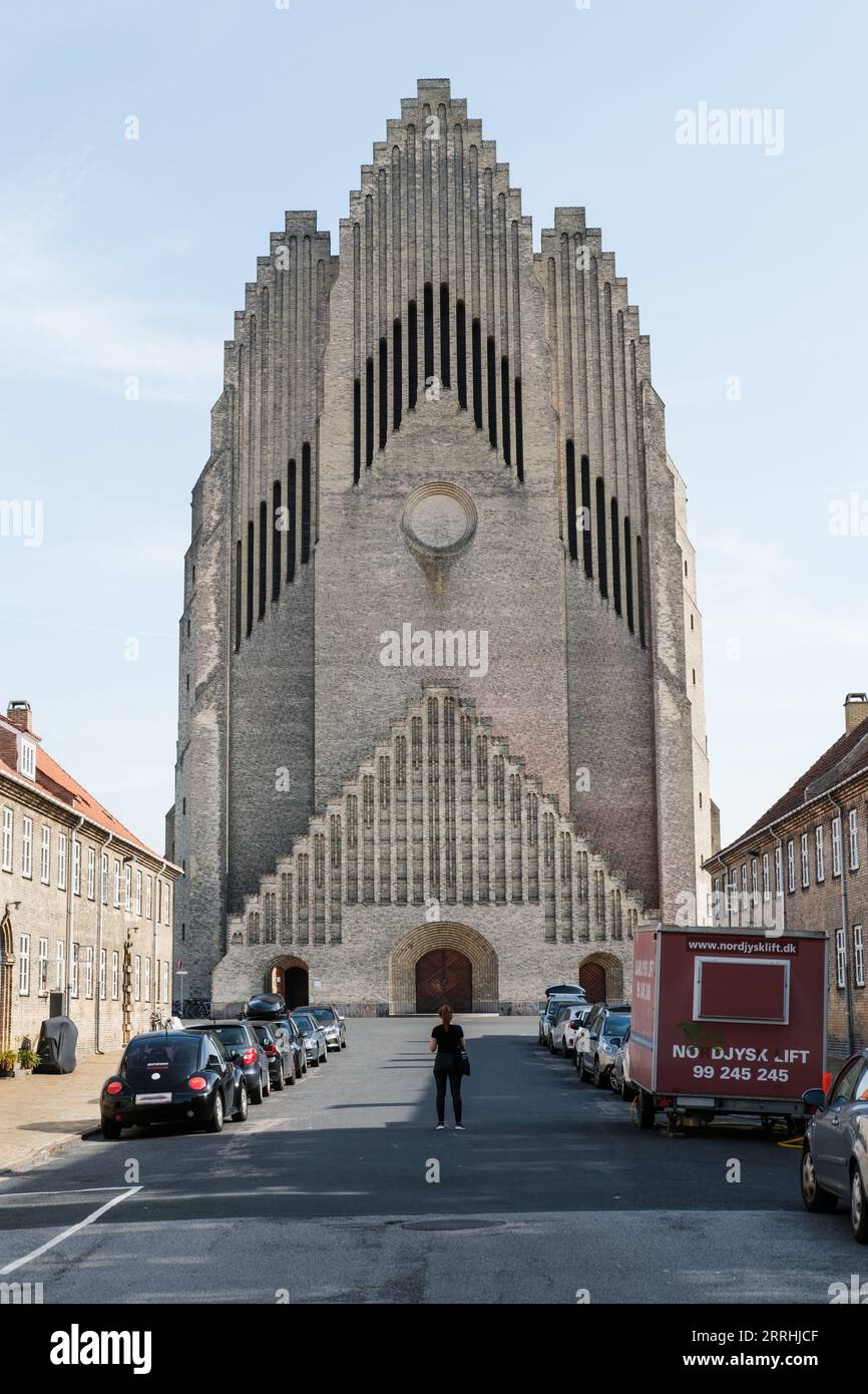 Façade of the Grundtvig's Church on midday with cars parked out front and a single woman standing in the middle of the road Stock Photo