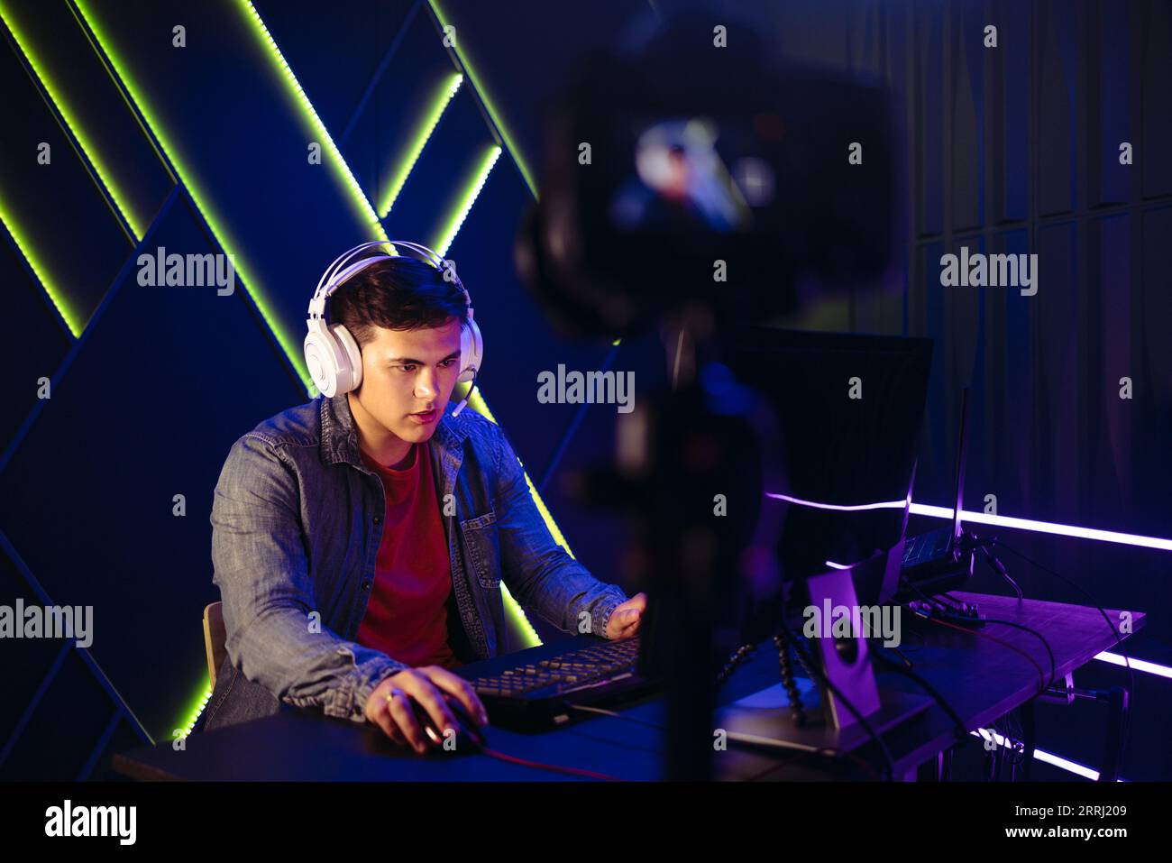 Young man sitting in front of a camera, live streaming a gaming session to an online audience. Fully engaged with the gaming world, he records every b Stock Photo