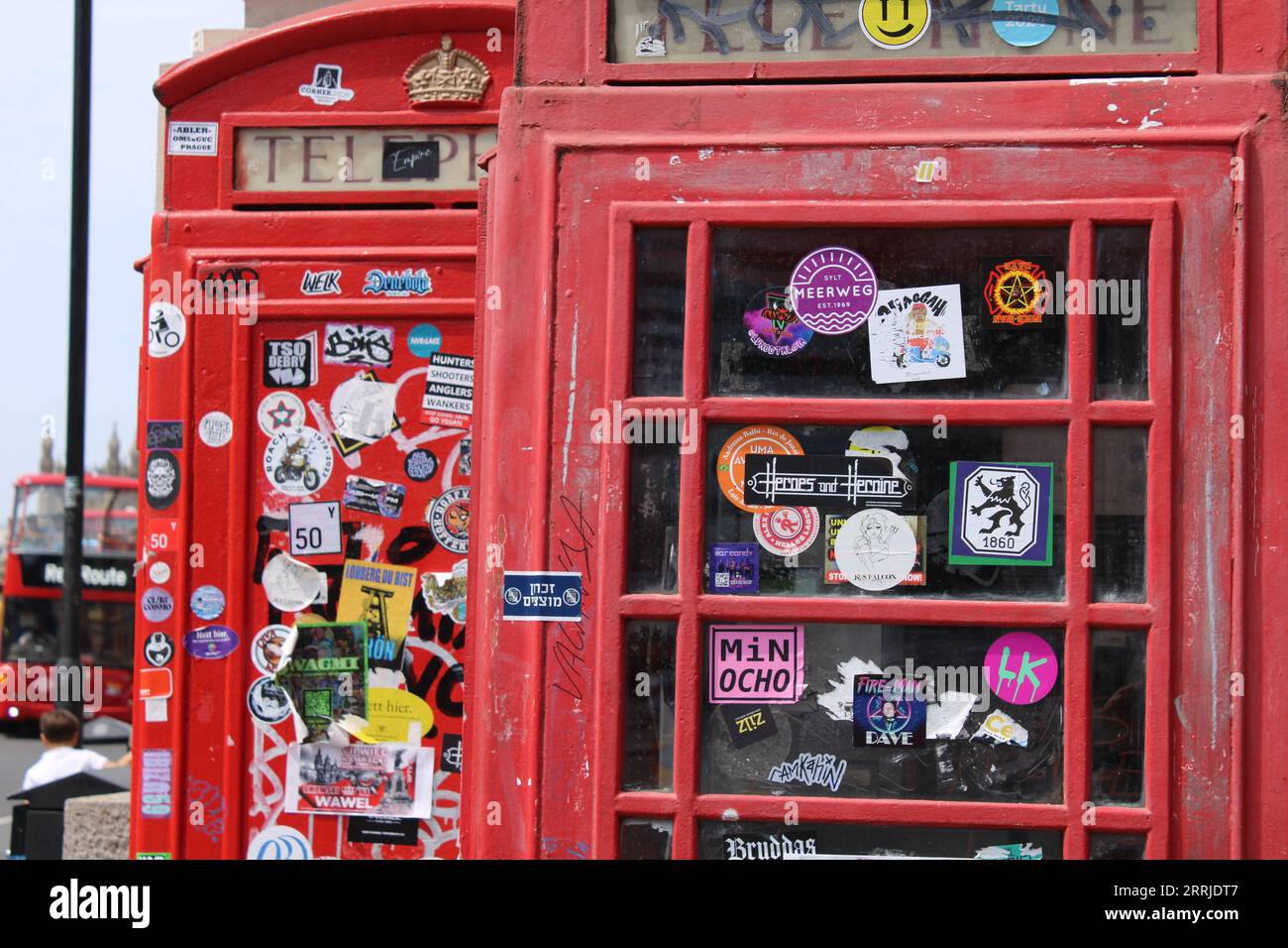 london red vintage telephone with a lot of stickers on it and a red bus in the background Stock Photo