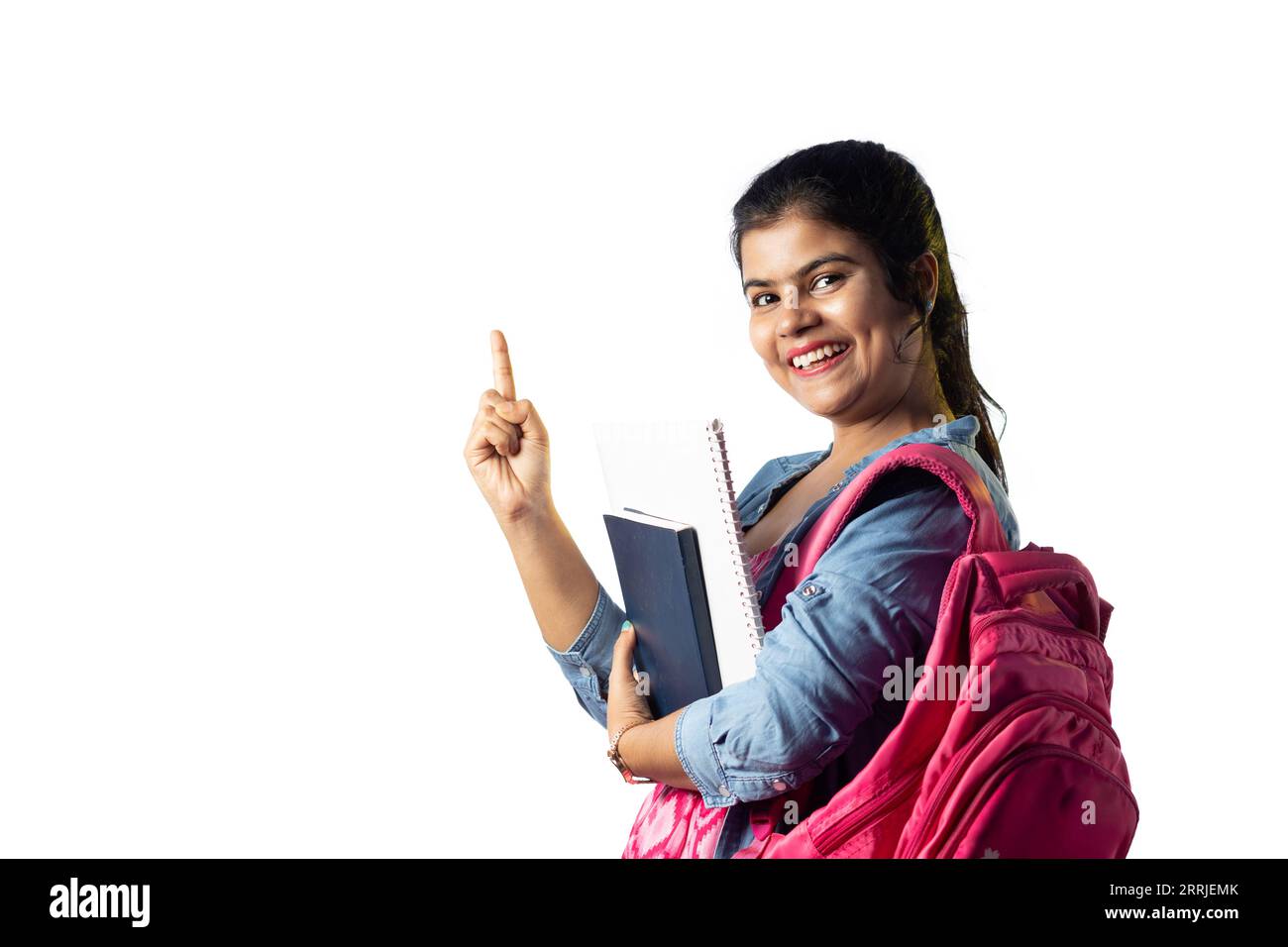 A pretty young Indian girl with books in hand and backpack pointing ...