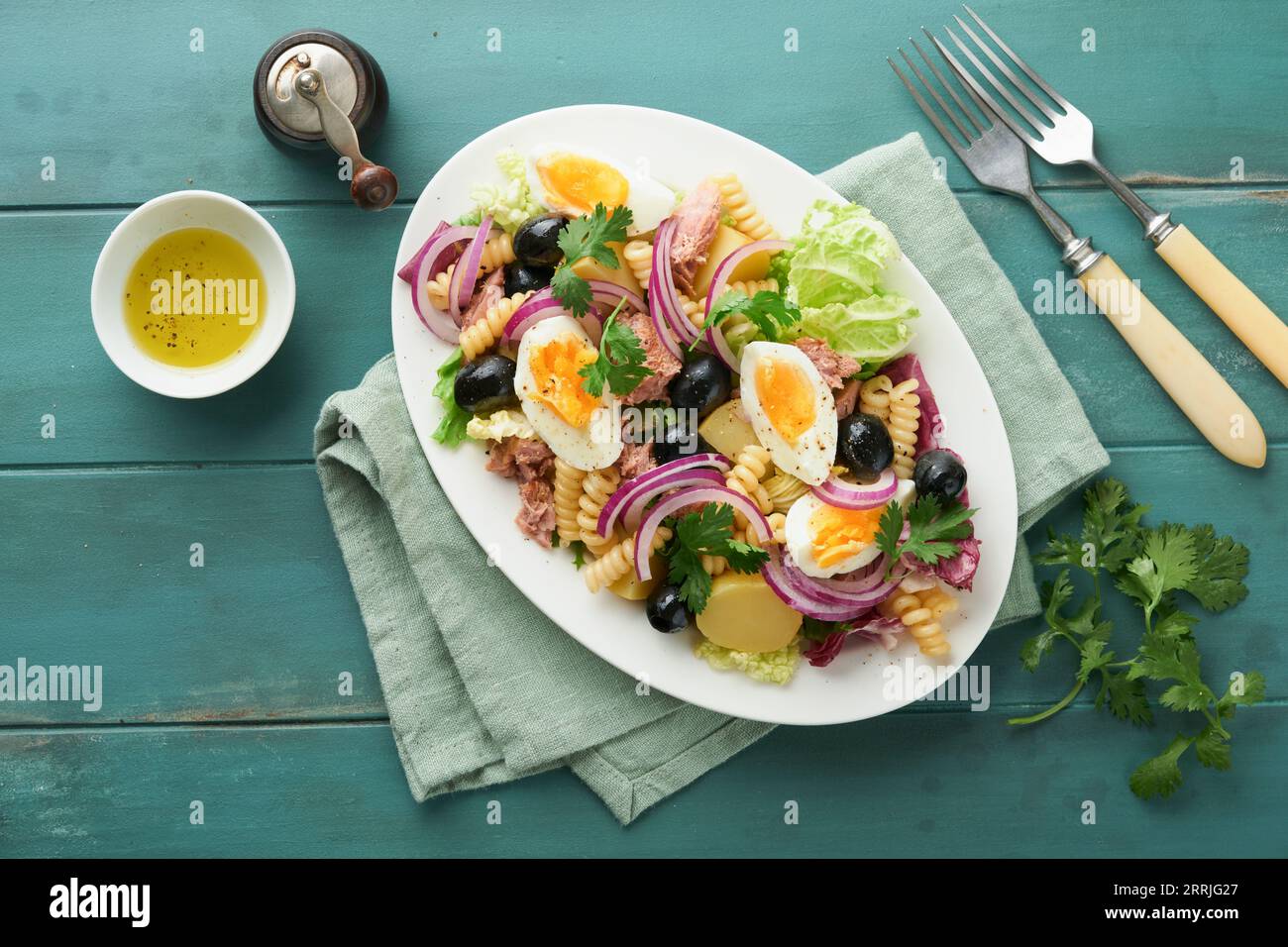 Tuna salad with pasta, eggs, potatoes, olives, red onions and sauce in white plate on old turquoise wooden rustic table background. Nicoise salad. Fre Stock Photo