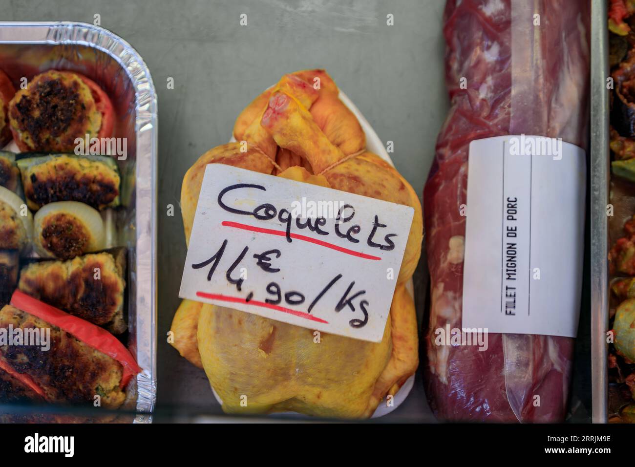 Whole cockerel or young male chicken carcass and pork loin at a butcher stall at the Cours Saleya farmers market in Old Town of Nice, South of France Stock Photo