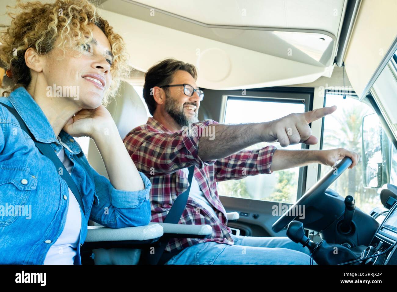 Happy couple of adult man and woman driving inside a camper van and enjoying alternative vehicle vacation together. Motorhome travel lifestyle and vacation on the road. People living adventure trip Stock Photo