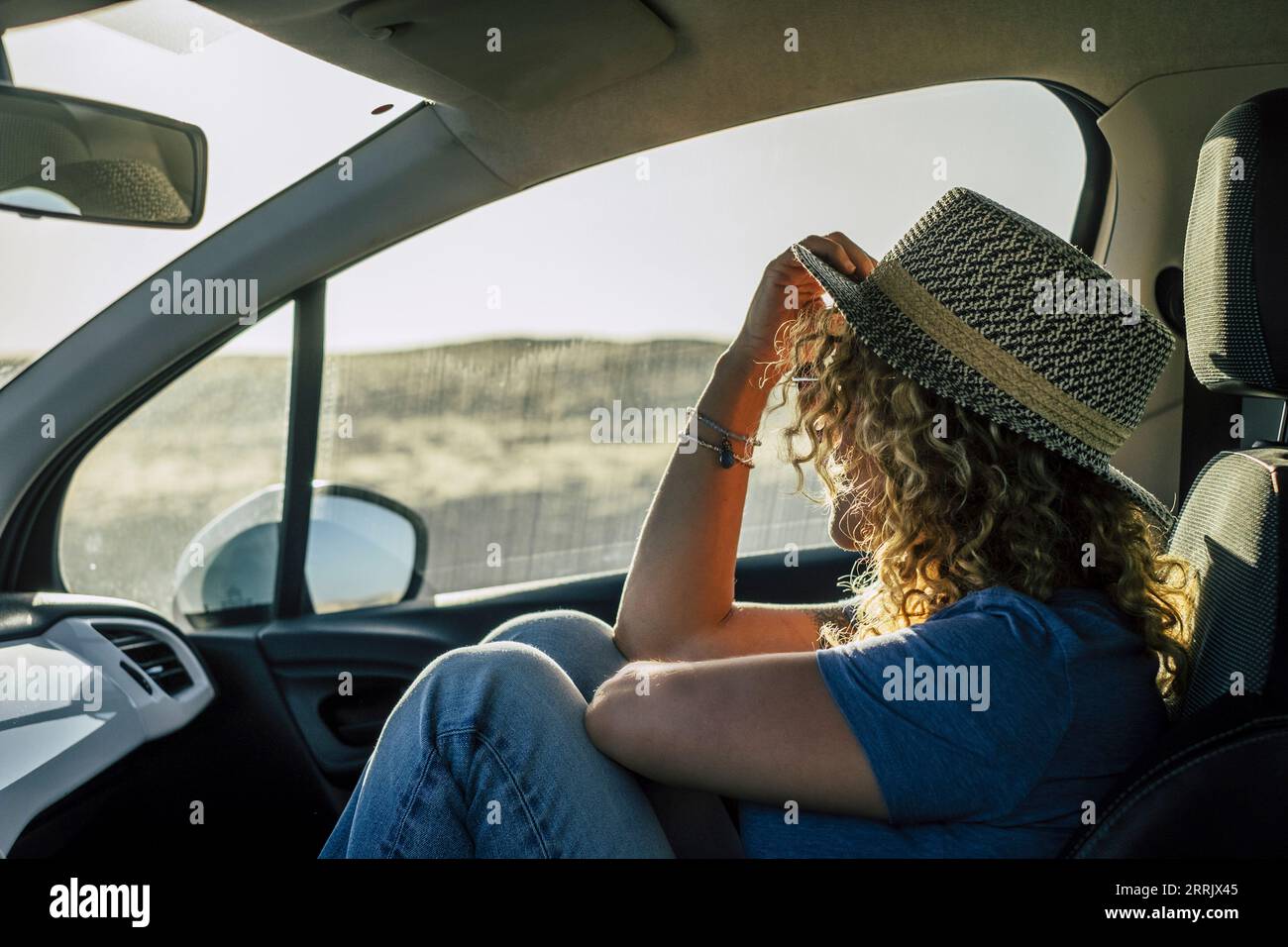 One woman sitting inside passenger car interior looking beautiful outside country side. Concept of travel people and transport. Free female in summer road trip adventure. Wanderlust and destination Stock Photo