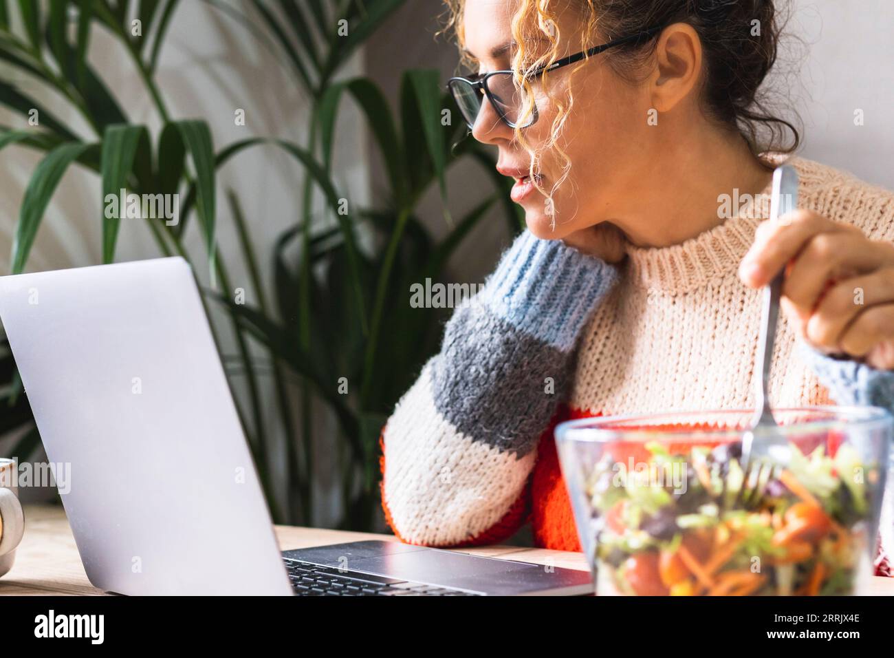Female employee working on laptop while eating a salads from glass bowl. Concept of professional freelance lifestyle and healthy nutrition. Lunch break and job business. woman in smart working indoor Stock Photo