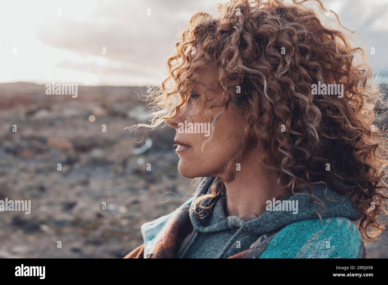 Side portrait of woman with long beautiful curly hair looking in front of her enjoying outdoor leisure activity. Travel and adventure people lifestyle. One adult female in travel desert experience. Stock Photo