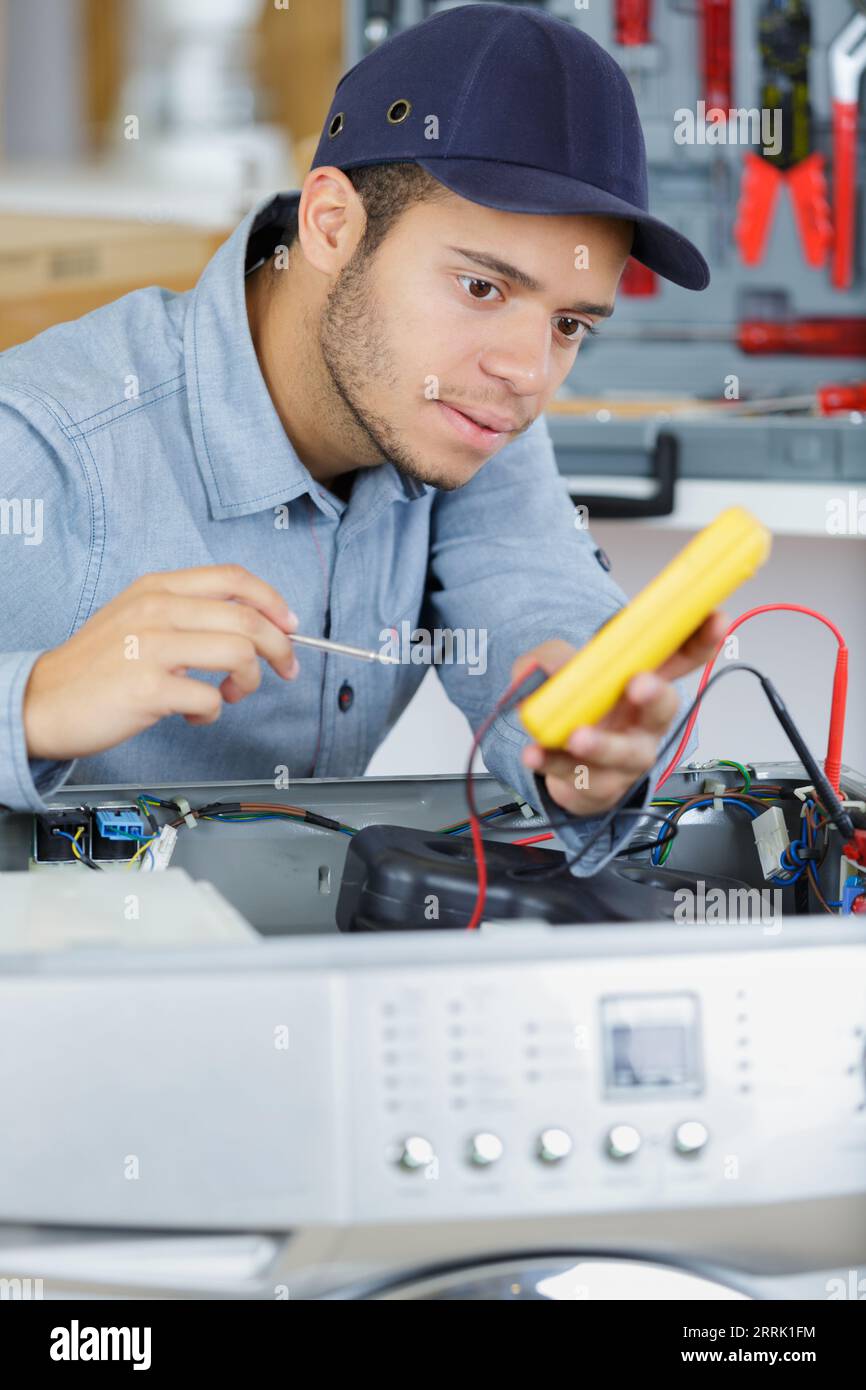 young serviceman testing washing machine with multimeter Stock Photo