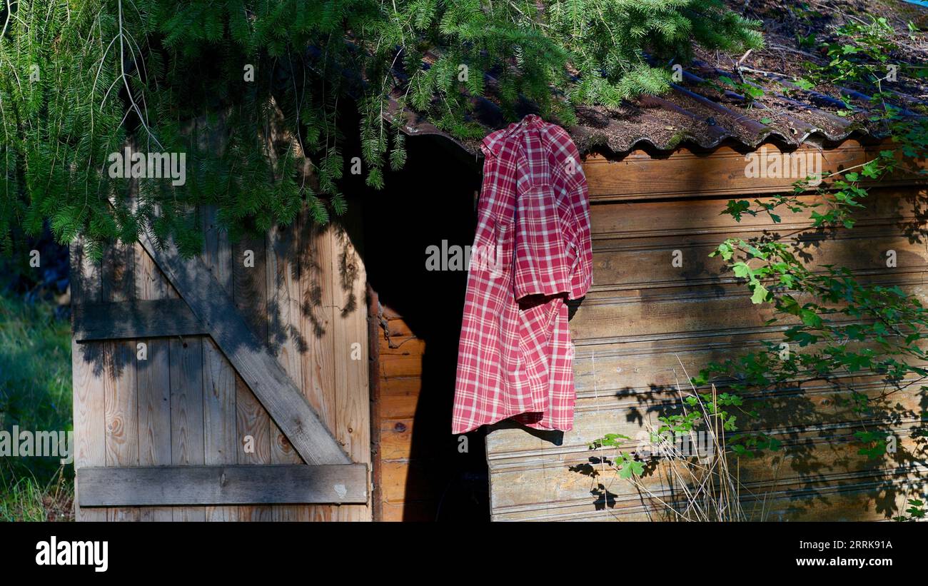 A short-sleeved red shirt hanging on a wooden shack. Stock Photo