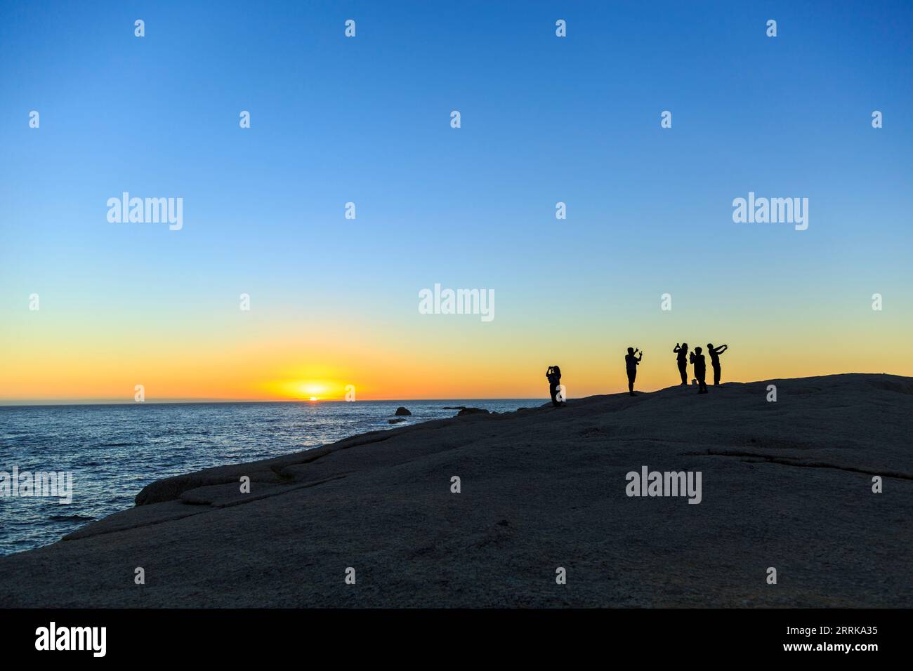 South Africa, Cape Town, sunset over the sea, rocks, silhouettes of a group of people taking selfies, Stock Photo