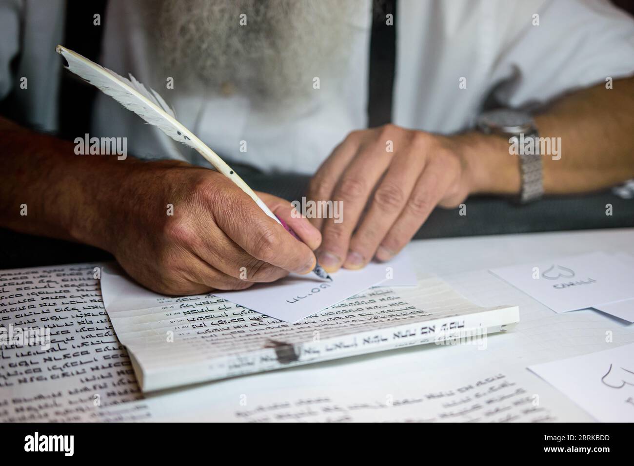 A mature male is seated at a desk, writing on a piece of paper with a quill pen Stock Photo
