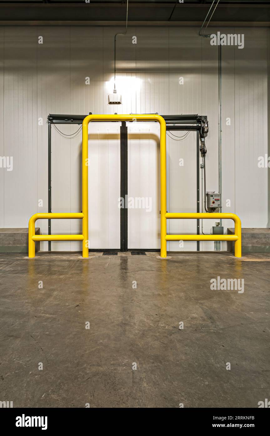 Sliding door to freezer from loading dock in a new cold-storage facility.  Yellow guardrails around doors to protect them. Stock Photo