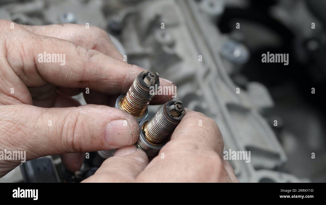 Extreme close-up of old mechanic's hands holding up old, damaged, corroded spark plugs Stock Photo