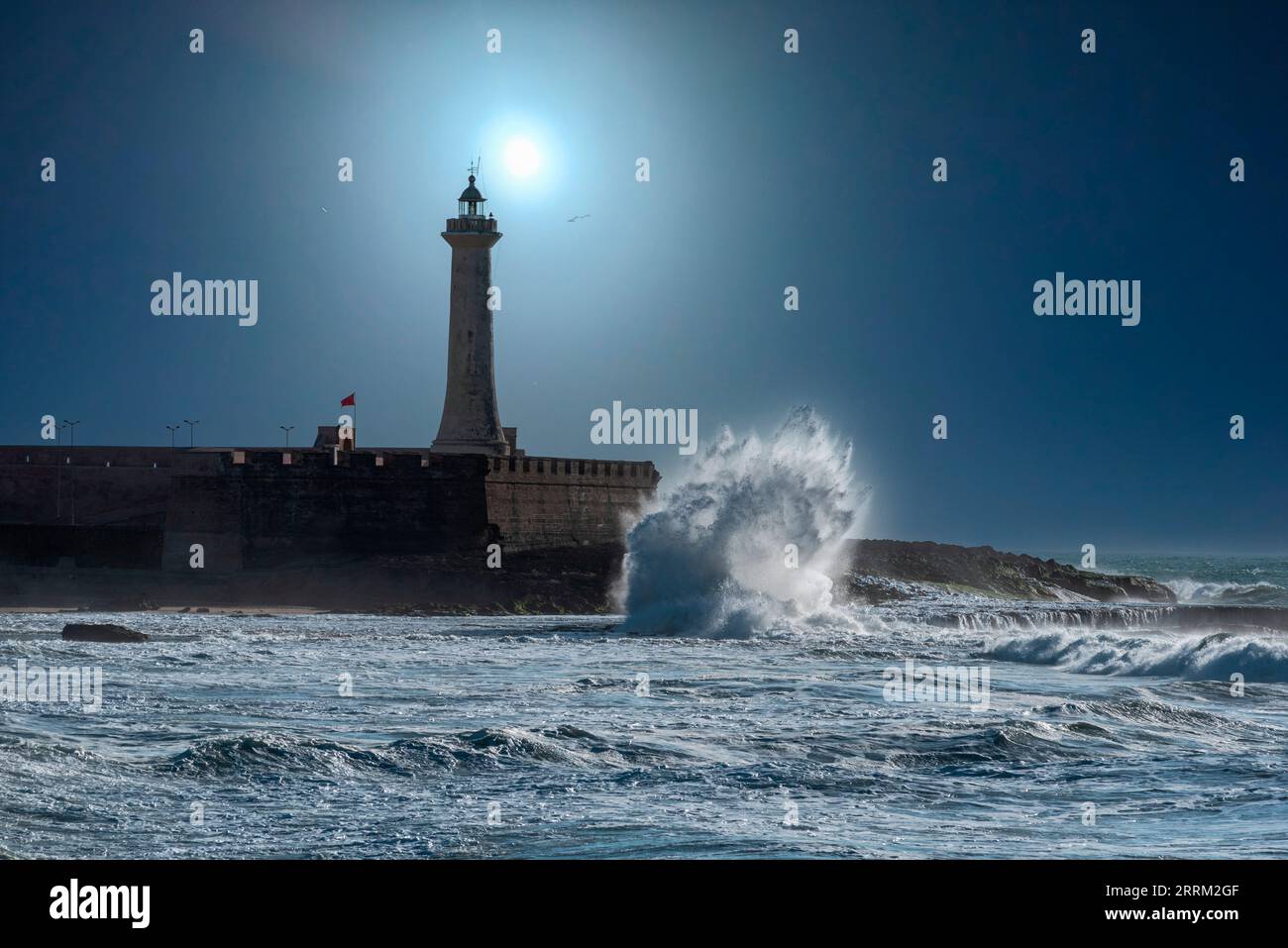 The moon shines over a picturesque lighthouse at night, waves break at the coast Stock Photo