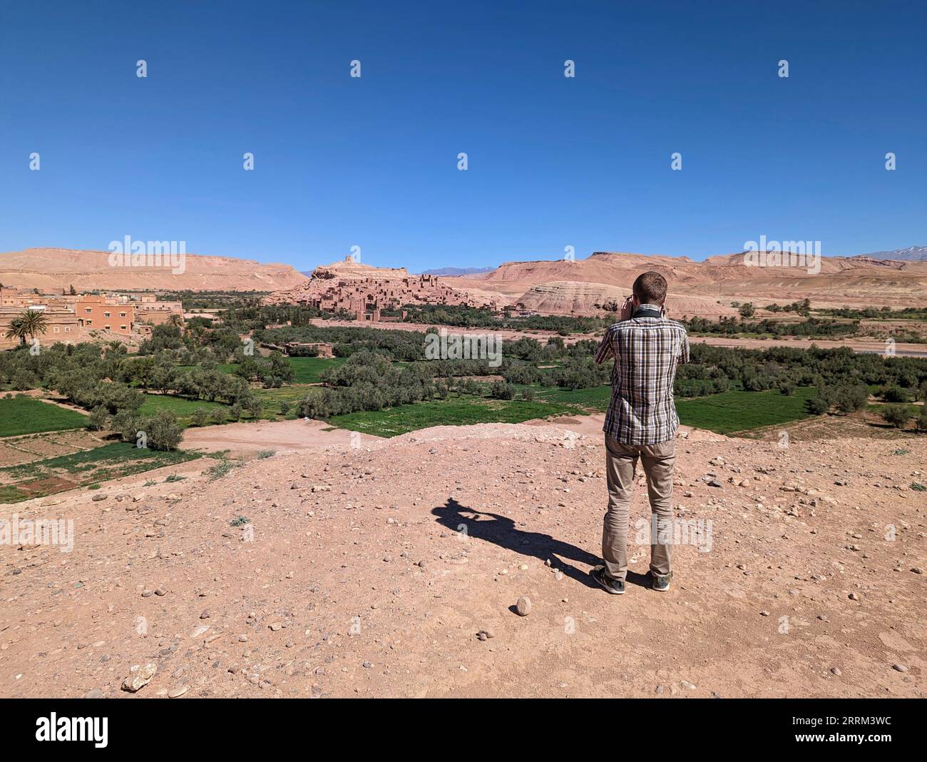 A tourist taking a photo from a famous viewpoint of the historic town Ait Ben Haddou in Morocco, famous berber town with many kasbahs built of clay, UNESCO world heritage Stock Photo