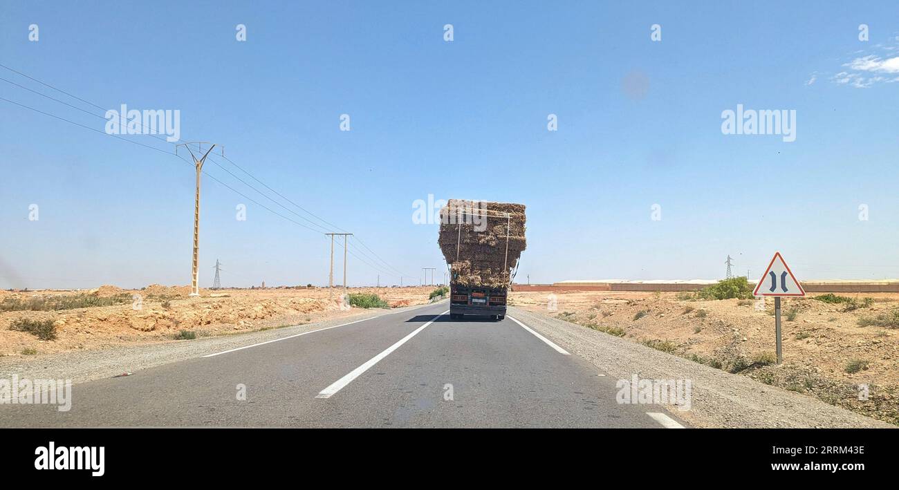 An overloaded truck driving through an arid landscape, Morocco Stock Photo