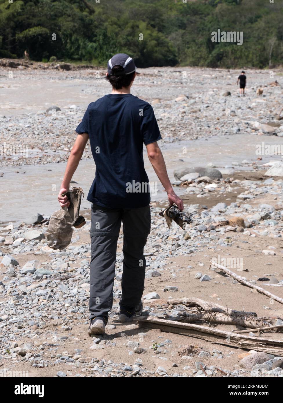 A young male waking on a river bed colecting solid waste for cleaning Stock Photo