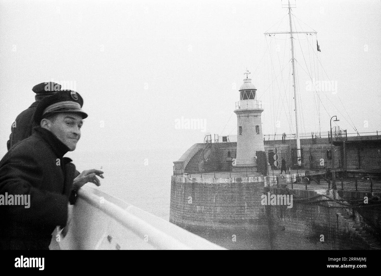 Kent. c.1960 – A French cross-channel ferry leaving Folkestone Harbour, passing the lighthouse at the end of the harbour arm. Two crew members are looking out over the side of the boat. Stock Photo