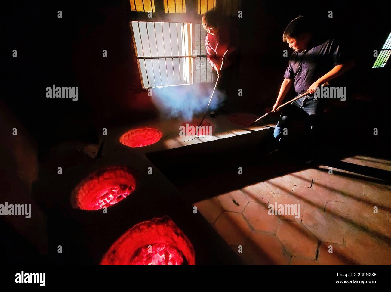 221202 -- WUYISHAN, Dec. 2, 2022 -- You Yuqiong L, the only female inheritor of Wuyi rock tea making technique, instructs her son Fang Zhou in the charcoal roasting technique of Wuyi rock tea in Wuyishan, southeast China s Fujian Province, May 10, 2020. Wuyishan, the hometown of rock tea, boasts a wide range of rock tea varieties. The making technique of Wuyi rock tea, a special oolong variety with a particularly roasted taste and floral and fruity aroma, is comprised of more than 10 processing procedures including tea harvesting, withering, fixation, twisting, drying and so on. Inherited and Stock Photo