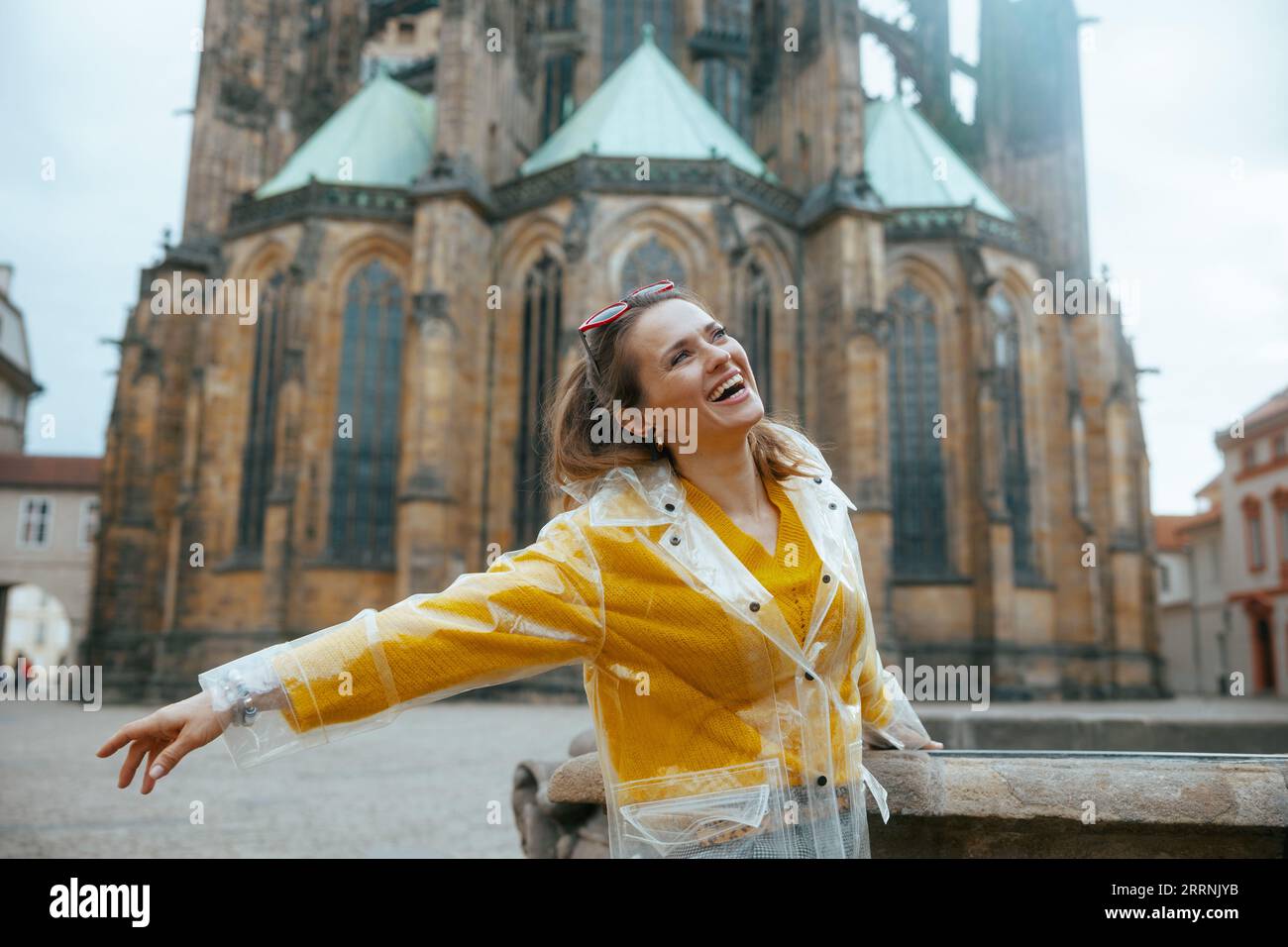 smiling stylish solo tourist woman in yellow blouse and raincoat in Prague Czech Republic enjoying promenade. Stock Photo