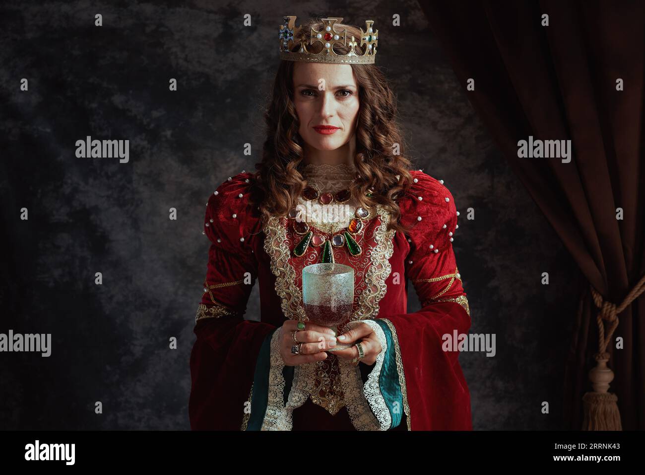 medieval queen in red dress with goblet and crown on dark gray ...
