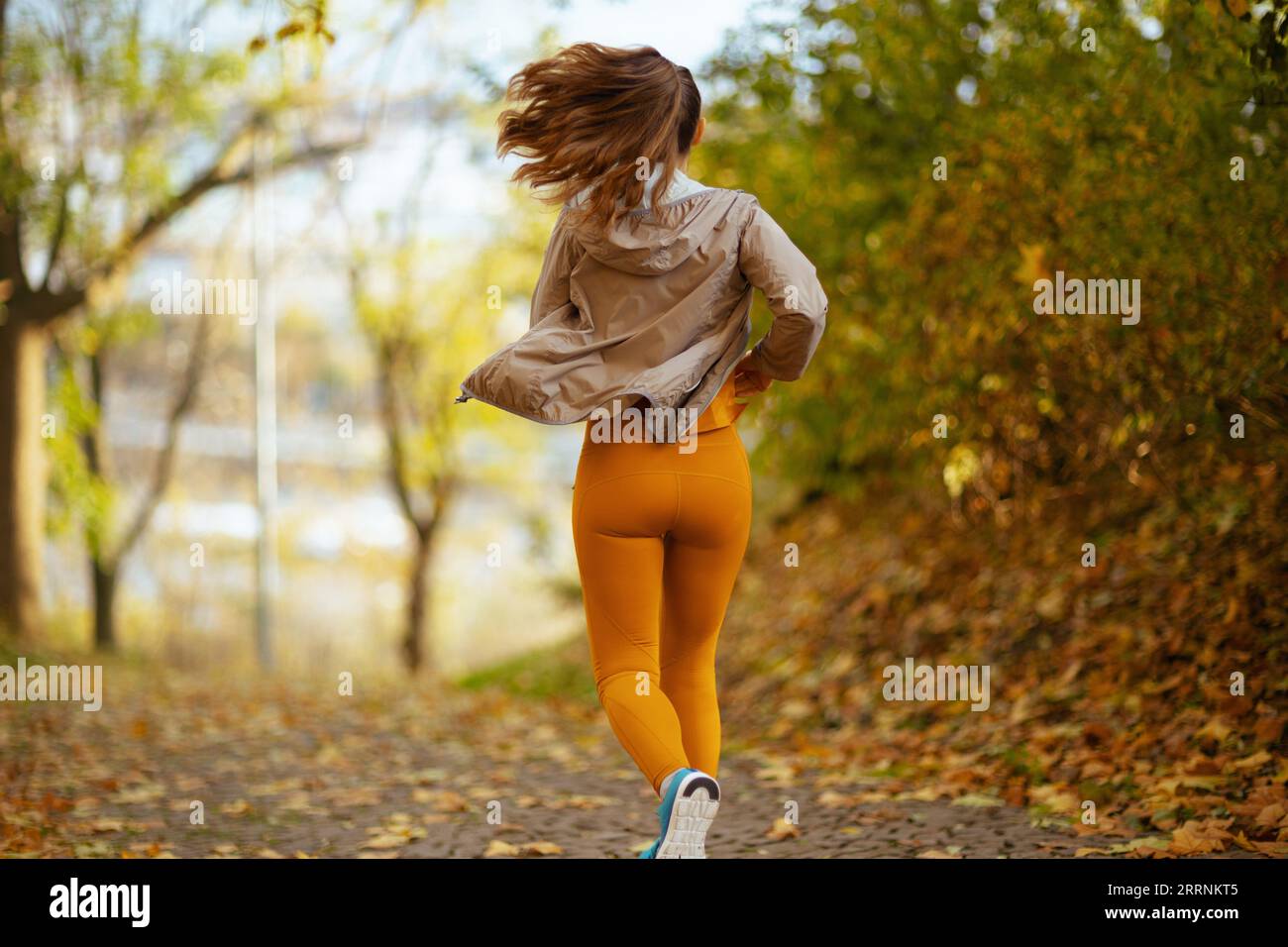 Hello autumn. Seen from behind woman in fitness clothes in the park ...