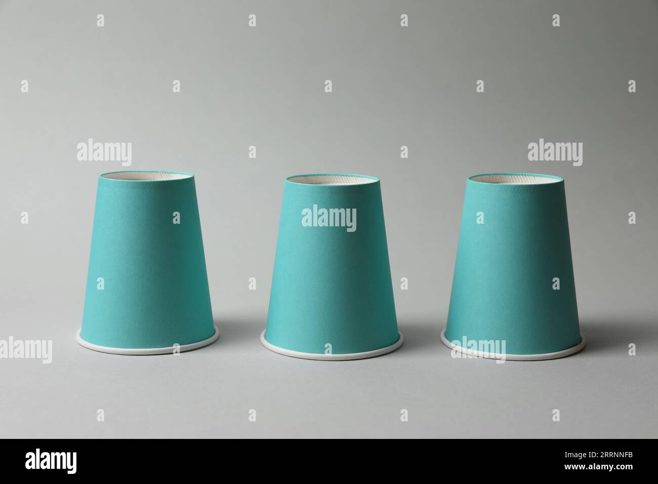 Three paper cups on light grey background. Thimblerig game Stock Photo ...