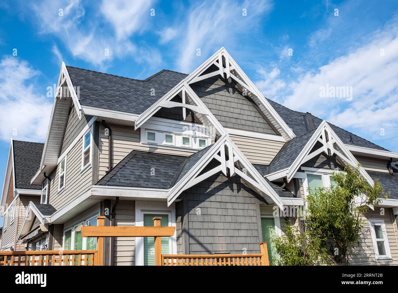 Houses with shingle roof against blue sky. Edge of roof shingles on top of the houses dark asphalt tiles on the roof. Beautiful roof work. Nobody, str Stock Photo