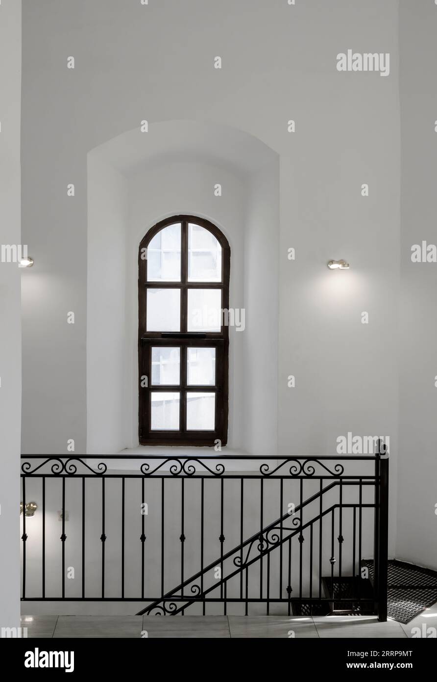 White walls with a black window frame and black iron railing stairs in the interior of a medieval bell tower Stock Photo