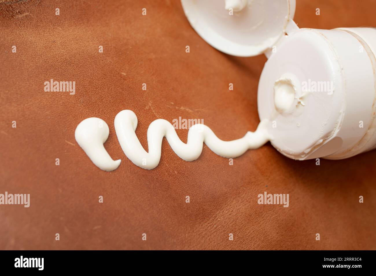 Applying white cream from an opened tube on brown leather , soft focus close up, abstract backdrop Stock Photo