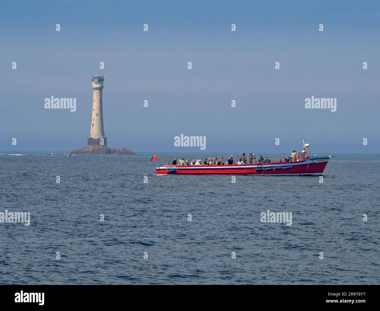 Tourist boat with the Bishop Rock Lighthouse in the background on a calm day, Isles of Scilly, Cornwall, England, UK Stock Photo