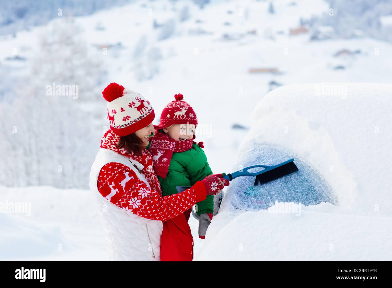 Mother and child brushing and shoveling snow off car after storm
