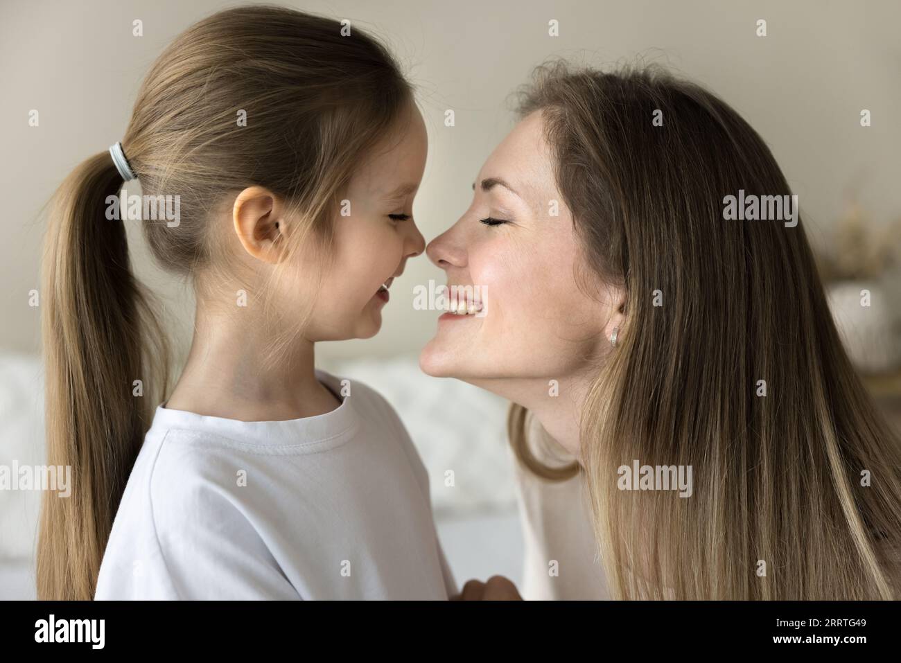Cheerful loving mom kissing pretty little daughter kid with faces Stock Photo