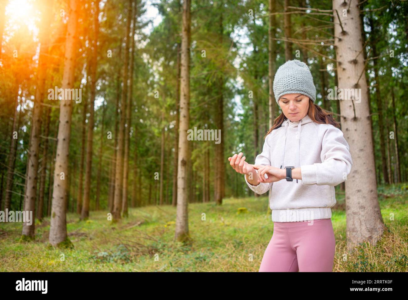 Fit sporty woman checking her smart watch fitness tracker, forest background. Stock Photo