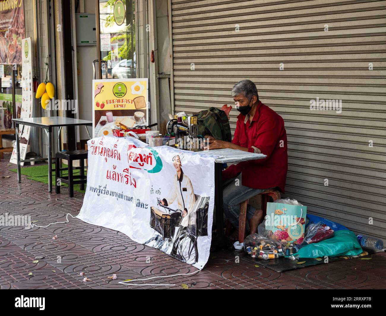 A skilled artisan passionately crafting garments with a sewing machine on a bustling Bangkok sidewalk, Thailand. Stock Photo