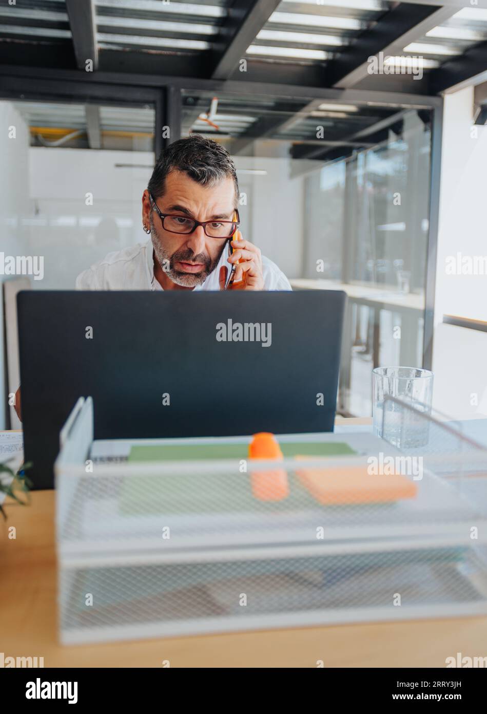 Senior or mature businessman having phone call while working on lap top at the office. Stock Photo