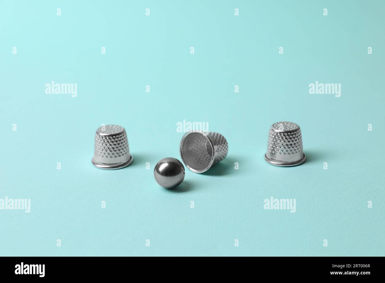 Metal thimbles and ball on light blue background. Thimblerig game Stock ...